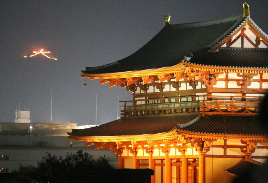 ［写真］「奈良大文字送り火」 は火床の数を半分にして行われた（左上）。右側は平城宮跡の朱雀門＝15日午後8時10分ごろ、奈良県奈良市で
