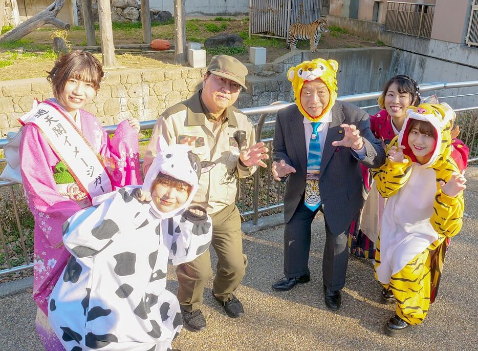 [写真]トラが後ろで見守る？中、天王寺動物園の向井猛園長（左から3人目）と通天閣観光の西上雅章会長（同4人目）がダジャレ口上を述べた。着ぐるみ姿のスタッフも場を盛り上げた＝23日、大阪市天王寺区で（提供：通天閣観光）