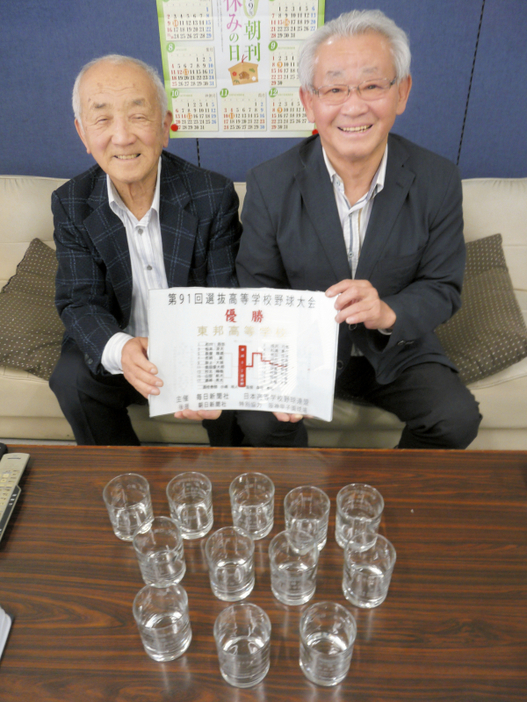 完成した優勝盾を手に笑顔を見せる松田忠雄さん（左）と吉川進司さん。選手や監督の名前を記したグラスも用意した＝毎日新聞四日市支局で