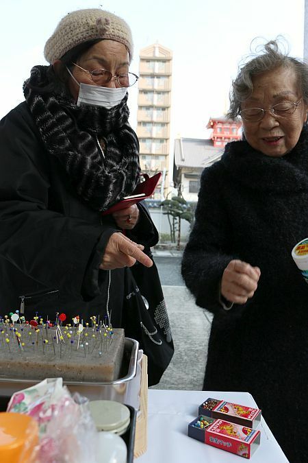 [写真]マッチやおかしの箱につめてきた針をコンニャクに刺し供養する人たち＝8日午後2時半ごろ、大阪市天王寺区で