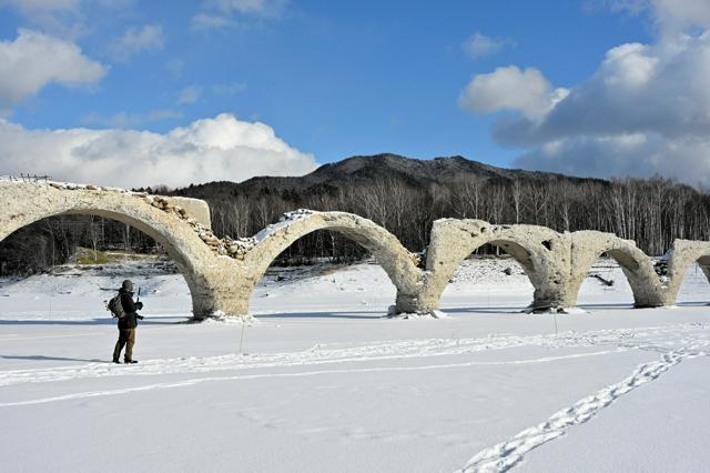 湖面が凍る前に、壁崩落部分が湖面上に姿を現したタウシュベツ川橋梁。左から1番目の橋脚上部のV字形に崩れた箇所が昨年6月に壁面崩落が起きた部分。特にここのアーチ部分の氷によるダメージが心配されていた。冬季は凍った湖を歩いて橋の近くまで行くことが出来る=2025年1月2日午後0時29分、北海道上士幌町