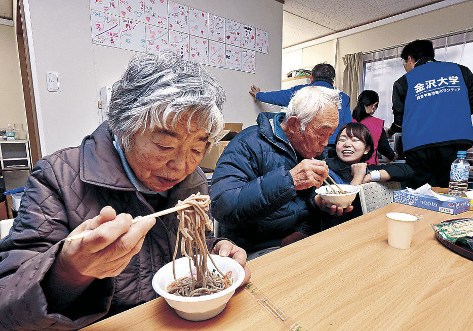 仮設住宅団地の集会所で、ボランティアと会話を楽しみながら、年越しそばをすする住民＝３１日午後０時１５分、輪島市杉平町