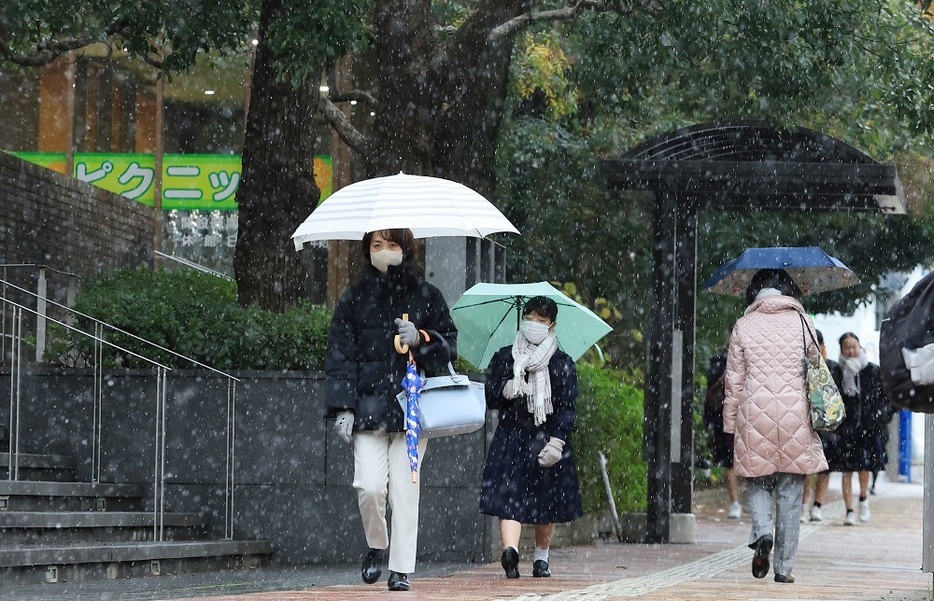 雪が舞う中、マフラーや手袋などで防寒して歩く人たち＝９日午後３時１９分、長崎市茂里町