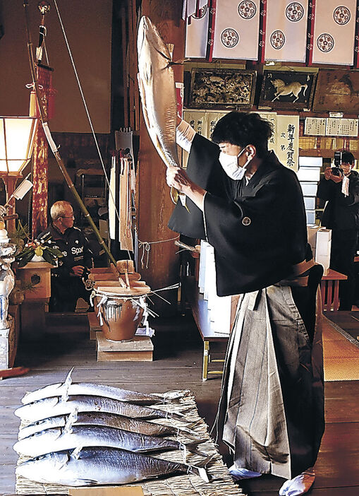 一年の平穏と幸を願ってブリを持ち上げる野口さん＝射水市の下村加茂神社