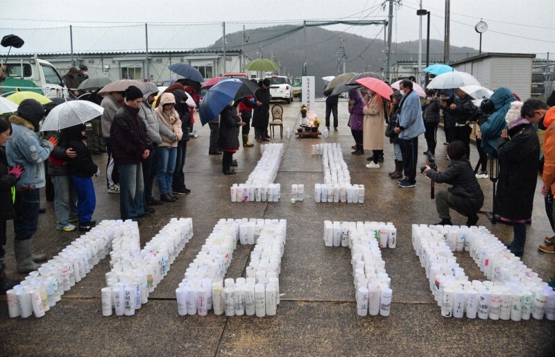 雨の中、仮設住宅の横で行われた追悼行事で、黙とうする住民やボランティアら＝石川県輪島市町野町で2025年1月1日午後4時10分、阿部弘賢撮影