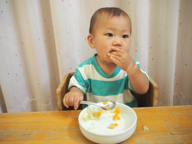 スプーンを持ちながら手づかみ食べをするあかちゃん