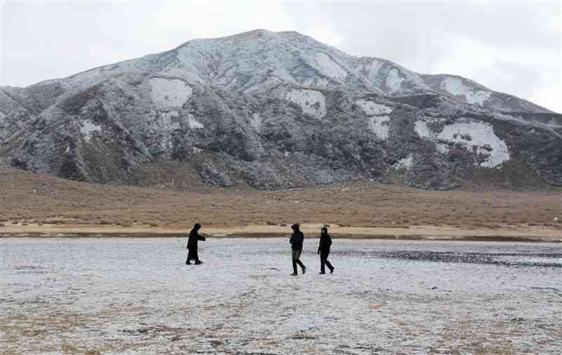 雪と氷に覆われた草千里ケ浜を楽しむ観光客ら。奥は烏帽子岳＝8日、南阿蘇村