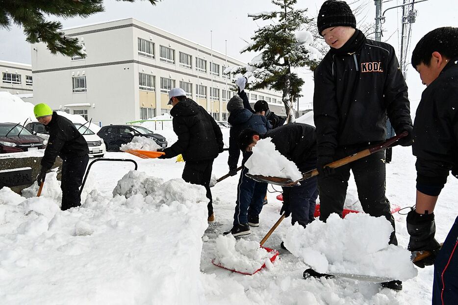 金沢小学校の前に積み上がった雪を崩して片付ける甲田中の生徒＝9日午前9時半過ぎ