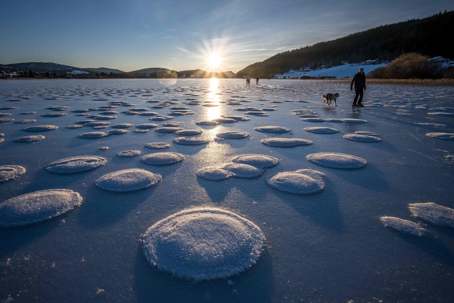 フランス中東部レルースで、凍結したルース湖の上にできたパンケーキ状の雪の間を歩く人々（2025年1月1日撮影）。【翻訳編集】 AFPBB News