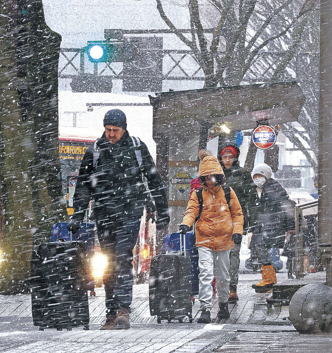 強い風雪に身をすくめながら歩く外国人観光客＝金沢市香林坊２丁目