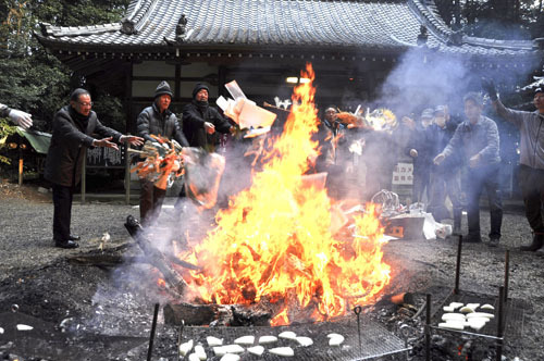 【鏡餅（手前）を焼きながら、かがり火にしめ飾りを投げ入れる参拝者ら＝四日市市波木町の加冨神社で】