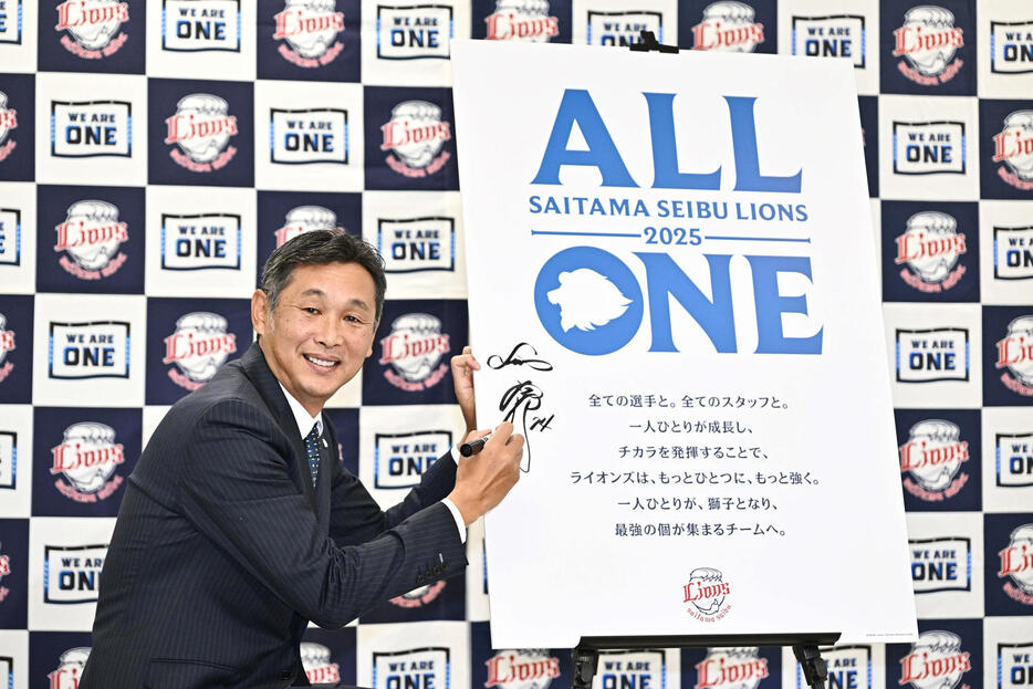 チームスローガン「ALL ONE」を発表しボードにサインする西武西口新監督（撮影・滝沢徹郎）