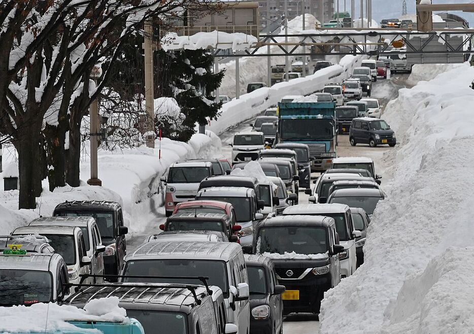 歩道側から雪の壁が迫り、通勤する市民などの車で混み合う青森市内の幹線道路＝6日午前8時57分、長島3丁目（写真は一部加工しています）