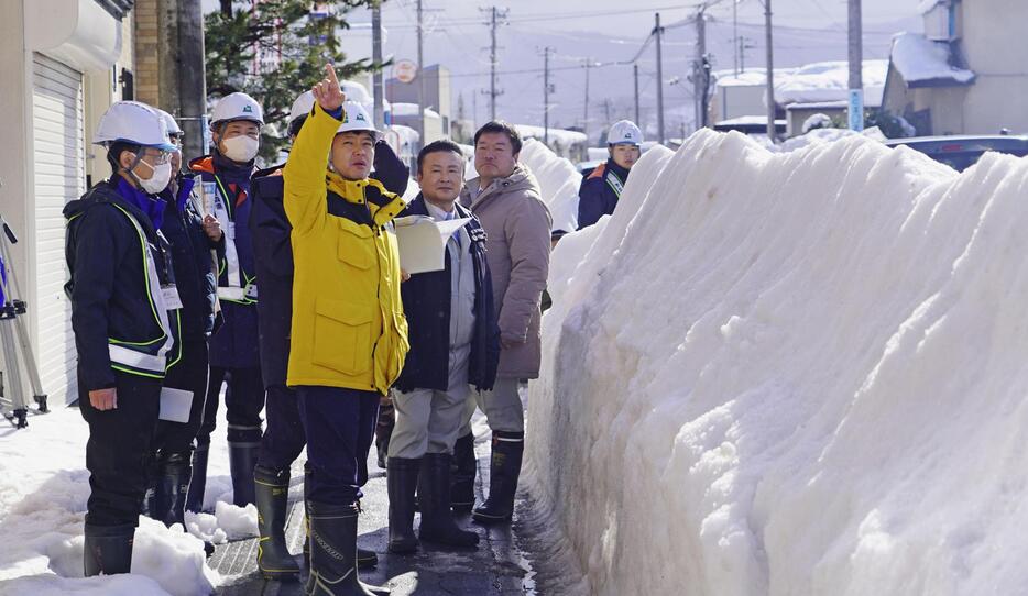 除排雪が滞る青森県弘前市を視察する宮下宗一郎知事（中央）。県道の両脇に雪の壁ができている＝7日午前