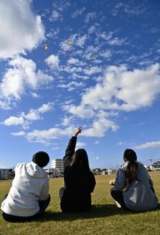 強い風が吹き、ぐんぐん上がるたこ揚げを楽しむ知念高校の小林夢奈さんら３人＝４日午前、与那原町・与那古浜公園（喜屋武綾菜撮影）