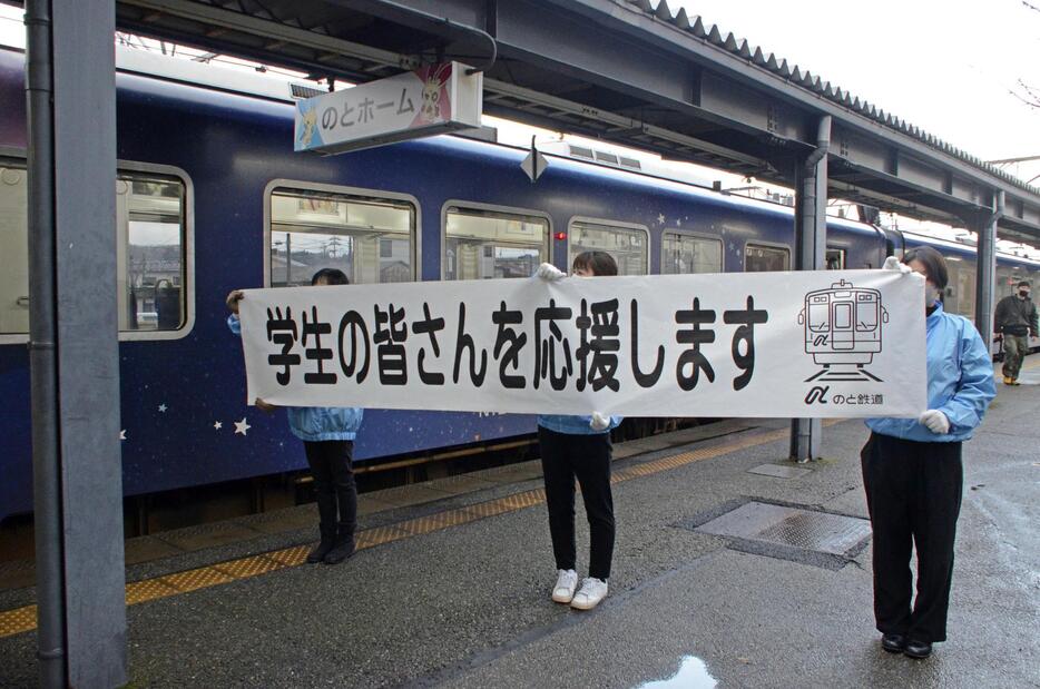 「のと鉄道」七尾駅で受験生を応援する横断幕を掲げる職員＝7日午前、石川県七尾市