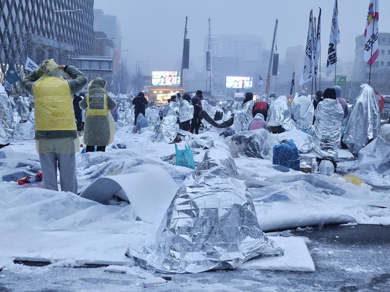 ５日、ソウル竜山区漢南洞（ヨンサング・ハンナムドン）の大統領官邸付近で開かれた弾劾要求集会で、雪の中で参加者がシルバーのビニールシートを覆ったり雨具を着たりしている様子。ソ・ジウォン記者