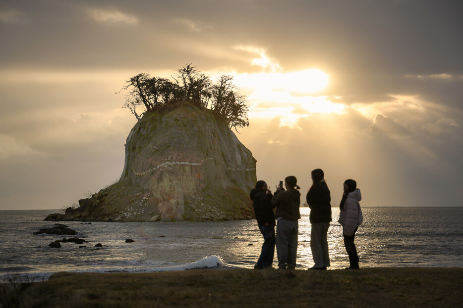 能登半島地震から１年を迎えた１日、景勝地「見附島」（石川県珠洲市）の奥に初日の出が見られた。幼なじみ４人で訪れた四辻美香さんは「今年は災害がない平和な１年になってほしい」と新年の願いを語った。