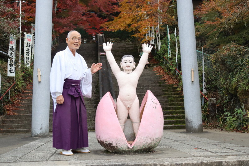 鳥居の前で来訪者を出迎える桃太郎の像。傍らに立つ宮司の若森国道さんが神社の歴史を説明してくれた＝愛知県犬山市の桃太郎神社で2024年12月11日午後0時15分、塚本紘平撮影