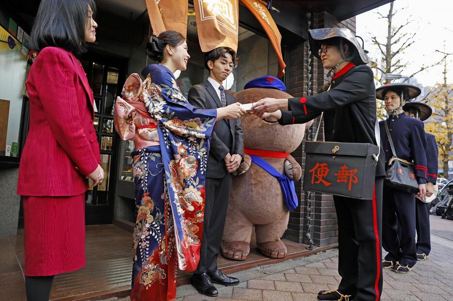 明治時代の制服で年賀状を手渡す配達員（右）＝1日朝、東京都新宿区