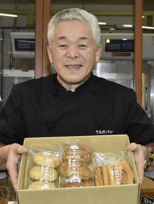 養殖マダイの骨の粉末を生地に練り込んだパンを手にする内田敏之社長＝2024年12月16日、松山市中央1丁目