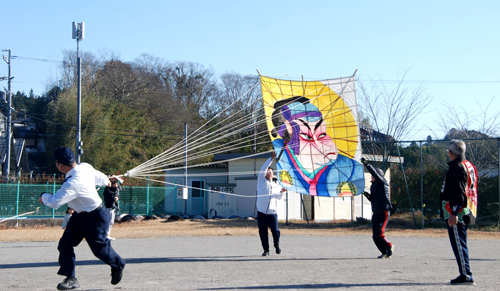 【大たこ揚げを指示する市川副会長（右端）＝亀山市両尾町の市立野登小学校で】