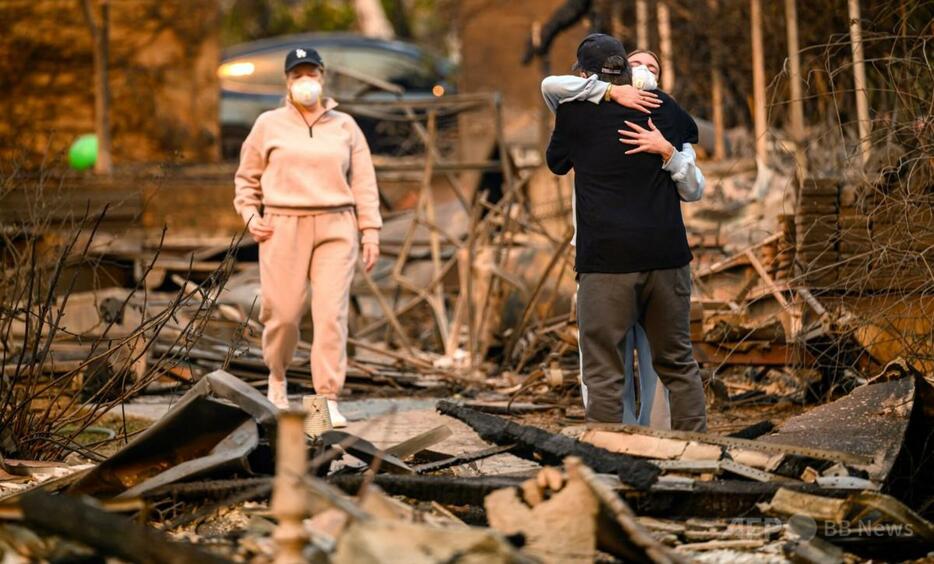 米カリフォルニア州ロサンゼルス郡アルタデナ地区で、イートン火災で焼失した自宅の焼け跡で、抱き合って泣く家族（2025年1月9日撮影）。【翻訳編集】 AFPBB News