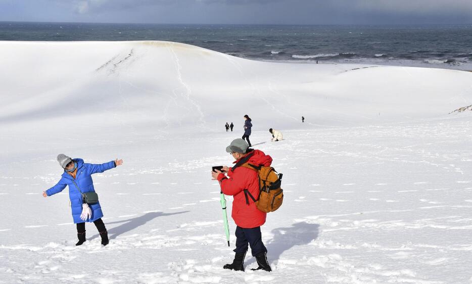 強い冬型の気圧配置が続き、一面が雪に覆われた鳥取砂丘で記念撮影する観光客。ねずみ色の雲の隙間から日差しが降り注ぎ、白銀の世界が広がった＝10日午前、鳥取市