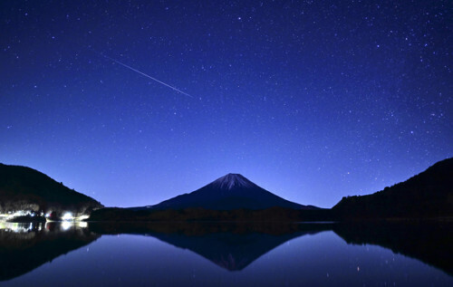 しぶんぎ座流星群がピークを迎え、精進湖の湖面にシルエットを浮かべる富士山の上に輝く流れ星（４日午前０時２５分、山梨県富士河口湖町で）＝上甲鉄撮影