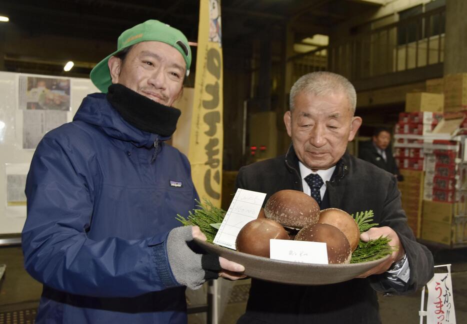 過去最高額で競り落とされた「のとてまり」を持つ仲買人の浅市佳男さん。右は「奥能登原木しいたけ活性化協議会」の樋下義勝会長＝9日午前、金沢市