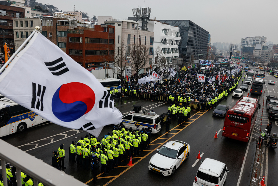 韓国の高官犯罪捜査庁（高捜庁）は１月６日、先月の戒厳令宣布を巡り内乱容疑で捜査している尹錫悦大統領の拘束令状の執行を委ねる旨の通知を警察に送ったと発表した。写真は大統領官邸に通じる道路を封鎖する抗議者らと、警官隊。５日、ソウルで撮影（２０２５年　ロイター/Tyrone Siu）