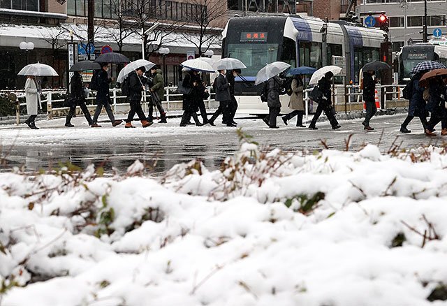 雪が積もる中、横断歩道を渡る人たち＝８日午前８時半ごろ、富山駅前