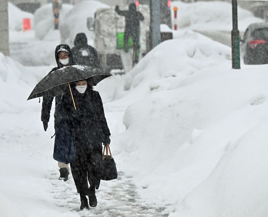 断続的な雪の中、再び積雪が増した歩道を行き交う市民＝8日午後2時20分、青森市北金沢1丁目