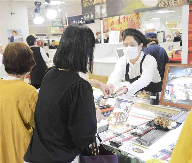 鶴屋百貨店が開いた物産展で、お釣りを受け取る買い物客。2025年3月以降はスマートフォンでも決済できるようにする＝24年、熊本市中央区