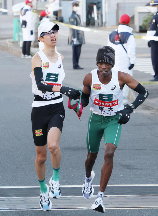 鶴見中継所を20位でタスキリレーする専大1区新井（左）と2区マイナ（撮影・河田真司）