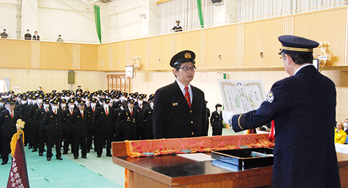 【櫻井市長（右）から表彰状を受け取る消防団員＝亀山市本丸町の市立亀山西小学校体育館で】