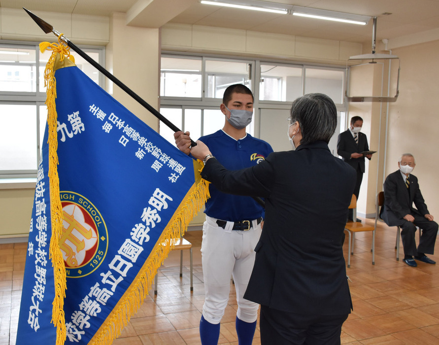 矢野正彦校長（手前）からセンバツ旗を受け取る石川ケニー主将＝茨城県高萩市石滝で２０２２年３月８日、長屋美乃里撮影