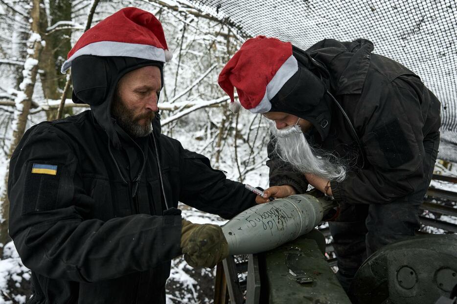 24日、ウクライナ東部ドネツク州バフムトで、砲弾にクリスマスのメッセージを書き込むウクライナ軍の兵士（ゲッティ＝共同）