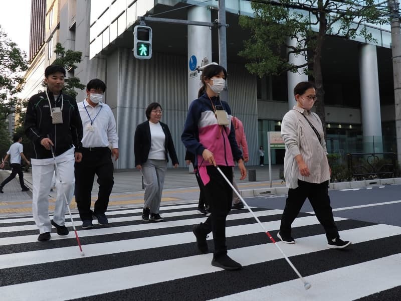 アイナビを起動したスマートフォンを首にぶら下げ、横断歩道を渡る宮崎さんら＝１０月１２日