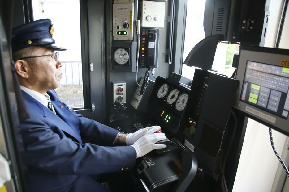 自動運転の走行試験で、緊急停止用ボタンに触れながら運転席に座る係員＝18日、和歌山市