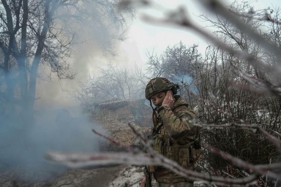 ウクライナ東部ドネツク州バフムト近郊で、りゅう弾砲の発射時に耳をふさぐウクライナ兵＝15日（ロイター＝共同）