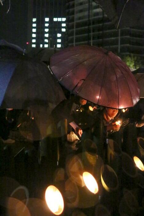 ［写真］雨の中、ろうそくの火を傘で守る人の姿が多く見られた＝17日午前5時45分ごろ、神戸市中央区で（撮影：柳曽文隆）