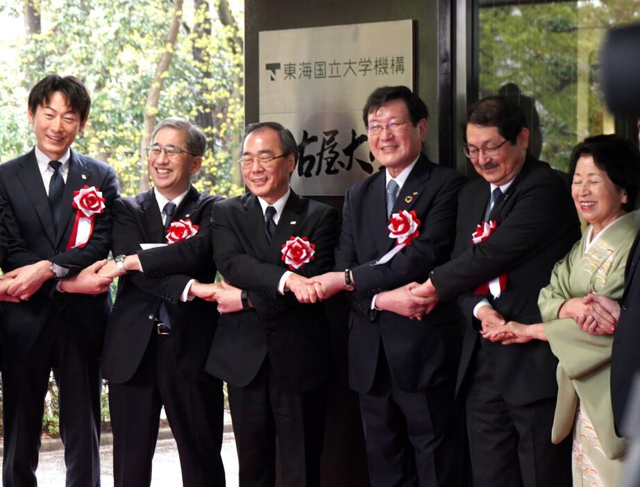 「東海国立大学機構」の看板を掲げて手を結ぶ名古屋大学の松尾清一総長（左から3人目）、岐阜大学の森脇久隆学長（同4人目）ら