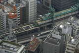 新幹線との重層部が終わる神田駅北側（秋葉原アプローチ部）を通る「靖国通り」の上では橋桁の設置が進む。ビルの合間からは東京駅へ向かう山形新幹線のE3系が顔を出す。遅れだったのか単独運転でやってきた（2013年3月30日、吉永陽一撮影）。