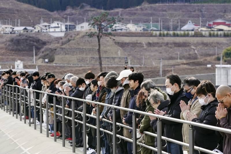 東日本大震災から１３年、地震発生時刻に合わせて黙とうする人たち。奥は「奇跡の一本松」＝３月１１日午後２時４６分、岩手県陸前高田市の高田松原津波復興祈念公園