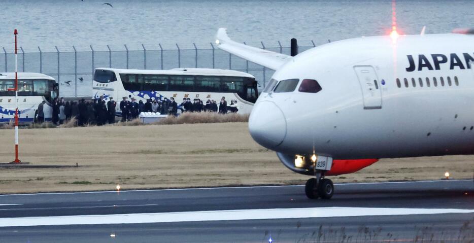 日航と海保の航空機による衝突事故から2カ月となり、事故現場の滑走路付近で献花する人たち（左奥）＝2日午後、羽田空港