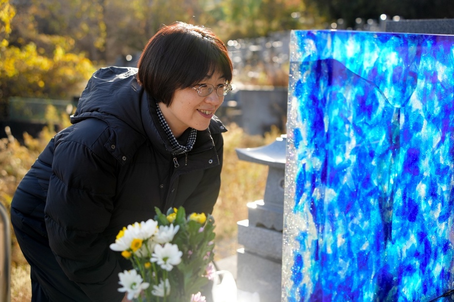 キラキラと光る水面のような墓石に話しかける畠山由紀子さん＝2023年12月、岩手県大船渡市、三浦英之撮影