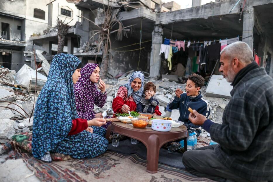 11日、パレスチナ自治区ガザで、破壊された建物のがれきに囲まれ、初日の断食明けの食事を取る家族（ゲッティ＝共同）