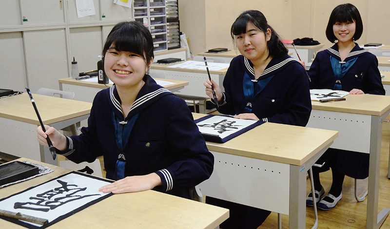 センバツ出場校の校名を書く武庫川女子大付属高の（左から）小西優羽奈さん、田邉春香さん、除本真理さん＝兵庫県西宮市の同校で、石川勝義撮影