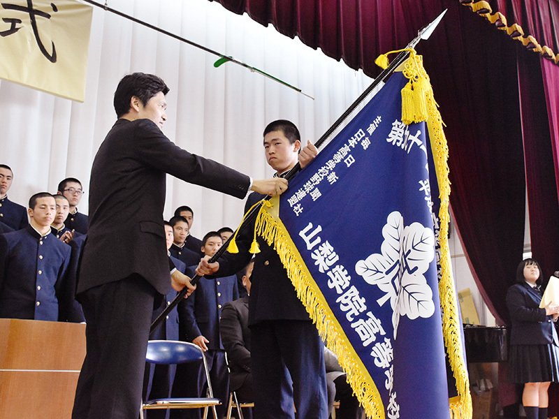 山内紀幸校長からセンバツ旗を受け取る山梨学院の相沢利俊主将＝甲府市酒折の同校で、金子昇太撮影